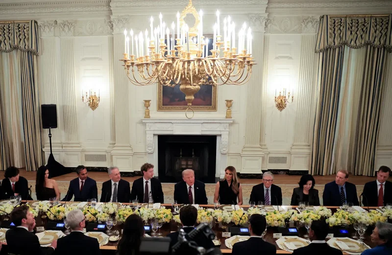 Donald and Melania Trump at dinner table with lots of mostly white, mostly men dressed up, with chandelier above them.