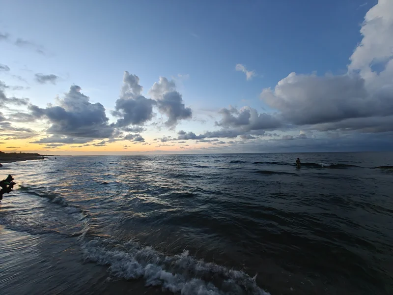 Beach at dusk, with dark blue sky and distant orange. Looming gray clouds.