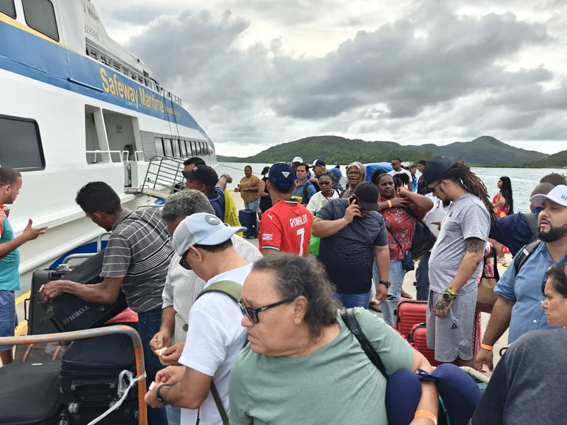 Many people crowded on dock next to ferry attempting to retrieve their luggage.