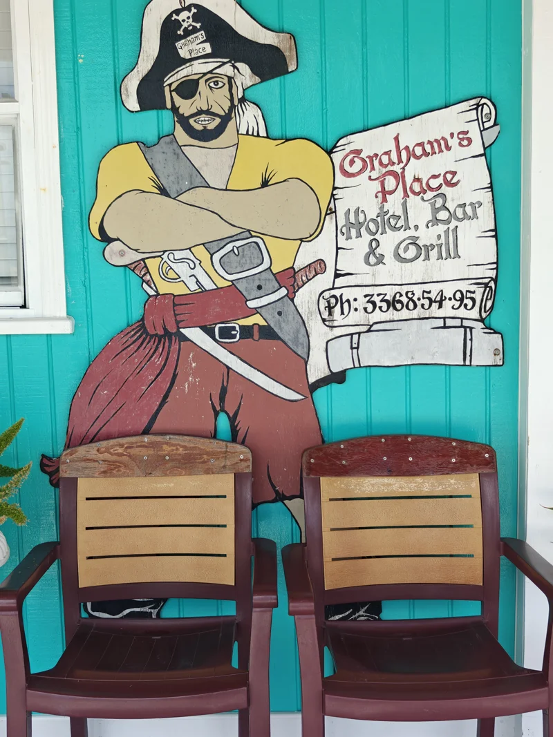 Signage of a pirate behind two empty chairs. Signage is for Graham's Place, Hotel, Bar, & Grill