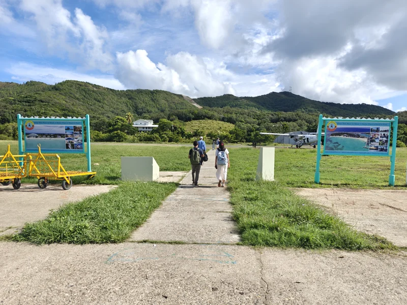 Man and woman walk toward airstrip with smally, white propeller plane in the distance.