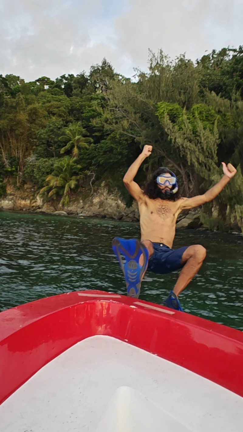 Silly man with long curly hair and snorkeling gear is falling backwards from red boat into water below.