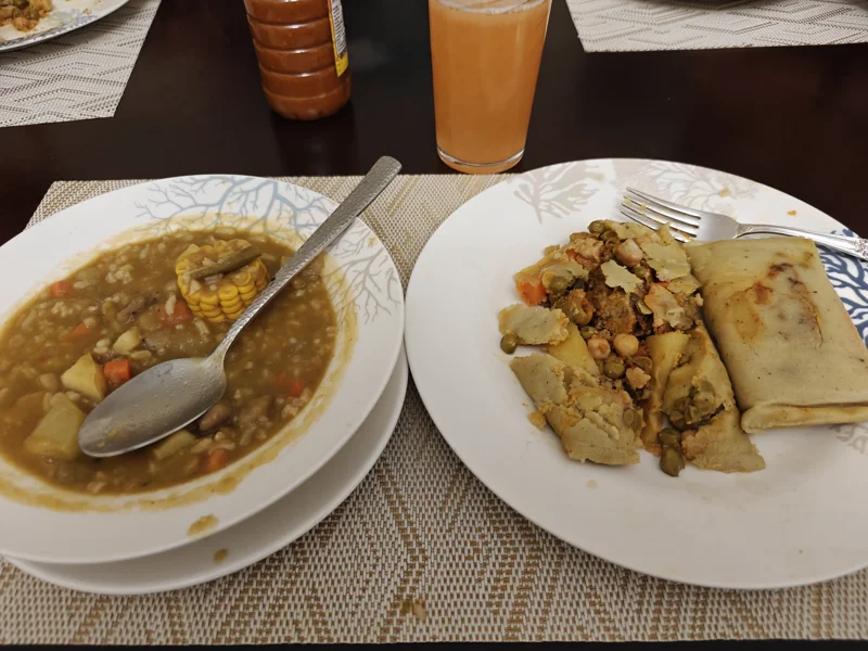One white bowl with lentils and a spoon next to a white plate with two tamales.