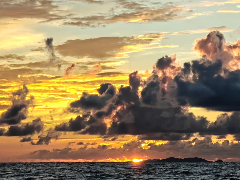 Fiery sky as sun sinks in the horizon. The clouds look dark and watercolored.