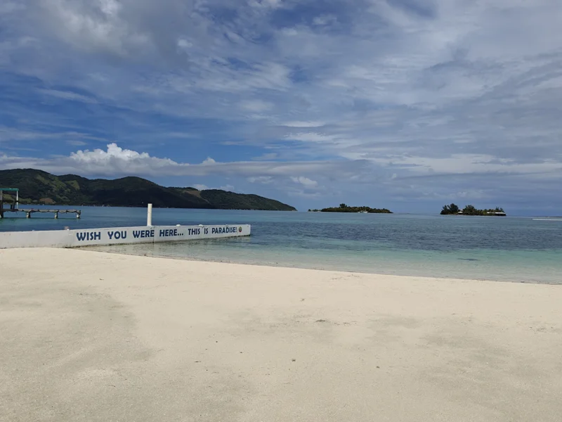 Empty beach. Clear water. Sign that goes out into water that says 'Wish You Were Here... This Is Paradise'