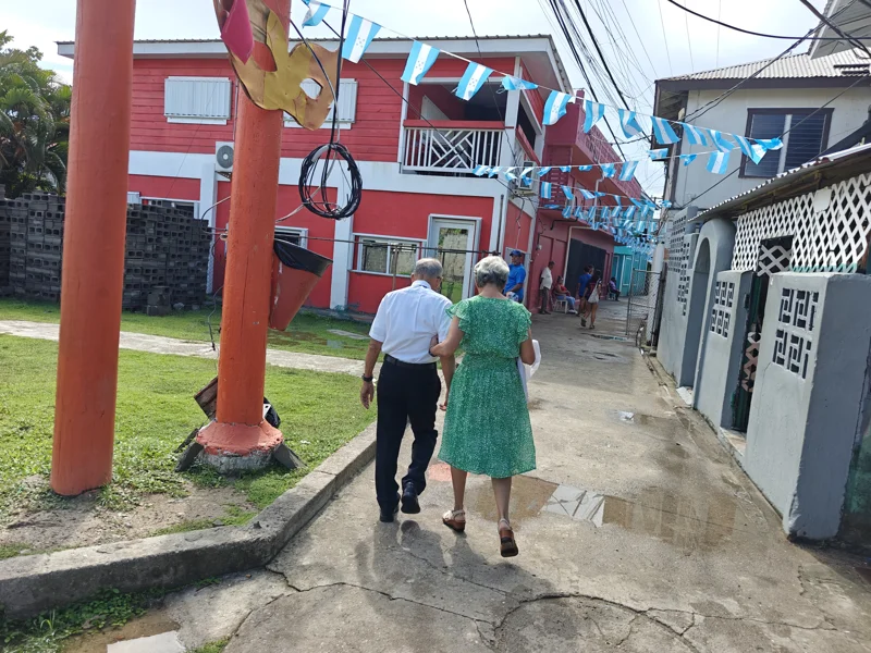 Dignified older couple walks through narrow walkway on top of cement, avoiding puddles.