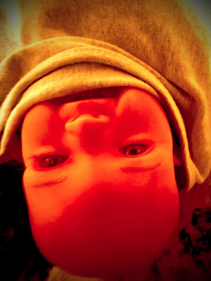Upside down baby doll face with blanket up to baby's mouth. Red hue.