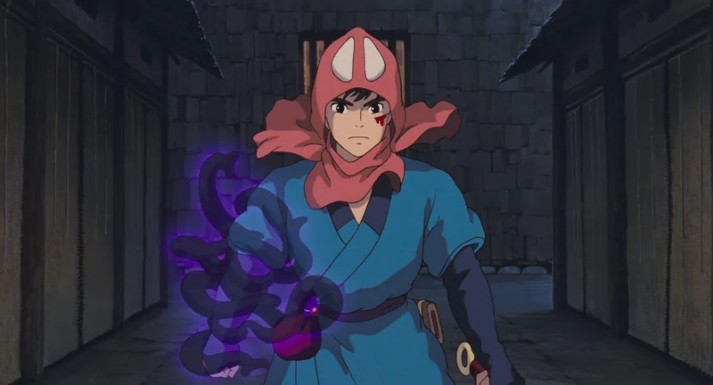 Man with red head covering and blue shirt walking forward, with what appears like translucent snakes around right arm.