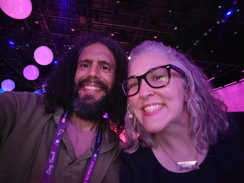 Selfie of man and woman in darkened conference room with pink orbs floating above.