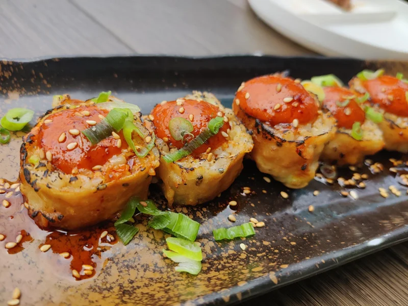Several pieces of sushi with red dragon sauce and sesame seeds on a long plate.